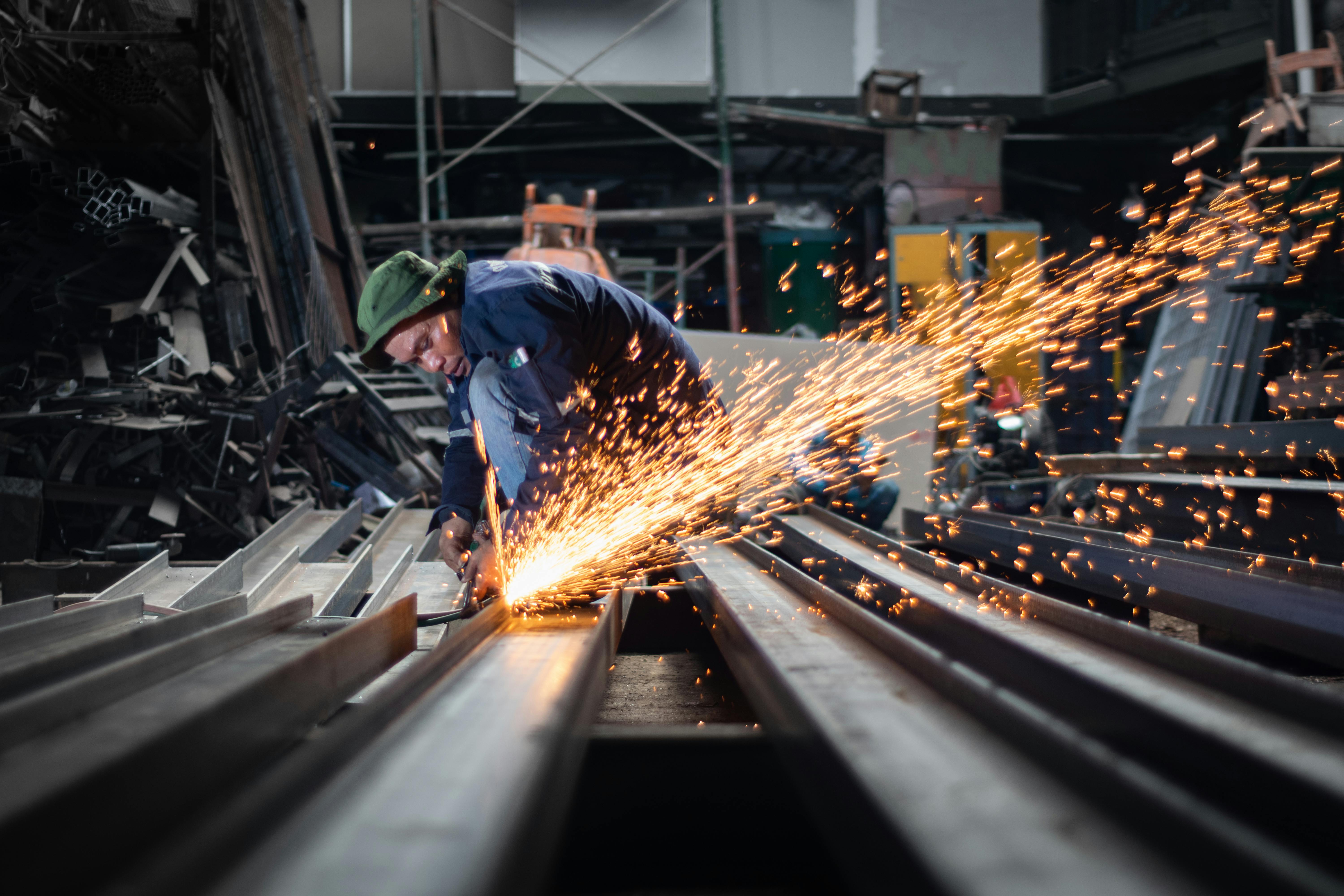 Welder grinding and cutting steel profiles with sparks in industrial environment